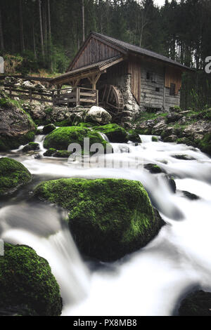 Idyllische lange Belichtung Blick auf eine alte verlassene Mühle mit bemoosten Felsen im wunderschönen Flussbett in einem mystischen Wald liegt an einem bewölkten Tag im Springtim Moody Stockfoto