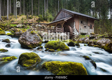 Idyllische lange Belichtung Blick auf eine alte verlassene Mühle mit bemoosten Felsen im wunderschönen Flussbett in einem mystischen Wald liegt an einem bewölkten Tag im Springtim Moody Stockfoto