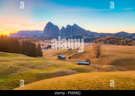Schöne Sicht der traditionellen Holz- Mountain Chalets an der malerischen Seiser Alm mit berühmten langkofel Bergspitzen im Hintergrund in Golden Morning Stockfoto