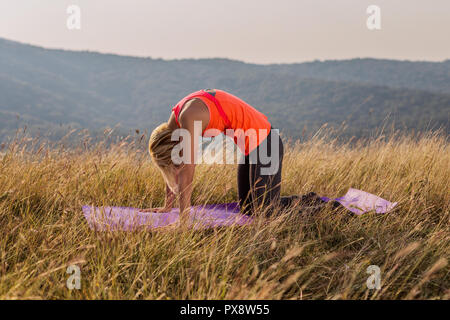 Schöne Frau Yoga in der Natur, in der Marjaryasana/Cat pose Stockfoto