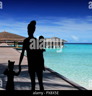 Familie Silhouette zu Fuß auf dem Pier von einem tropischen Resort am Meer eine Mutter mit einem kleinen Tochter halten sich an den Händen und tragen ein Baby Stockfoto