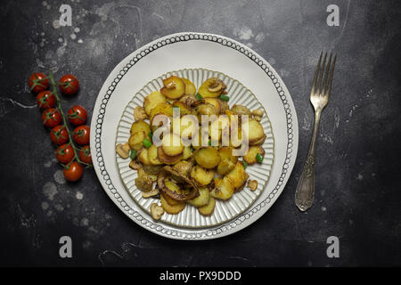 Tabelle Urlaubs zum Abendessen. Bratkartoffeln mit Pilzen und Zwiebeln auf schwarzen Hintergrund. Gabel und Kirschtomaten in der Nähe von Stockfoto