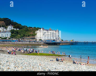 26. Juli 2018: Llandudno, Conwy, Großbritannien - Llandudno Strand an einem heißen Sommertag, und das Grand Hotel. Im Vordergrund steht die Kiesel See Defense. Stockfoto