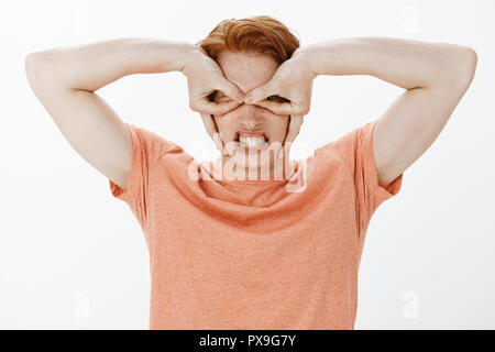 Guy Gefühl, wie Superhelden. Portrait von lustig, fröhlich und kindisch hübscher Junge mit Sommersprossen und roten Haare, so dass die Maske mit den Fingern über Augen, Aufeinanderpressen der Zähne, die beängstigend Gesicht beim Spielen mit Kindern Stockfoto