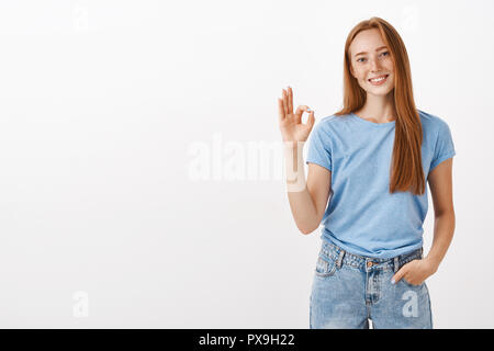 Ok kein Problem. Portrait von freundlich und fröhlich gut aussehende rothaarige Freundin mit Sommersprossen die Hand in der Tasche in beiläufigen Gespräch die Arbeit in der Zeit zeigen okay oder hervorragende Geste getan werden Stockfoto