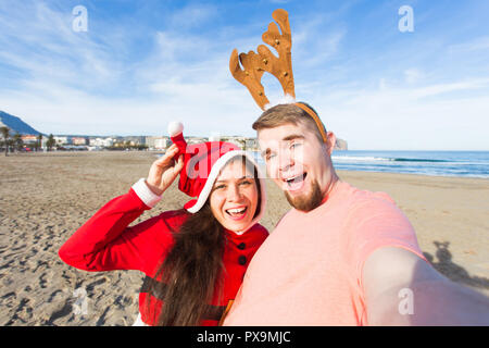 Spaß und Winterurlaub Konzept - glückliches Paar in Weihnachten Kostüme unter selfie über Sandstrand Hintergrund Stockfoto