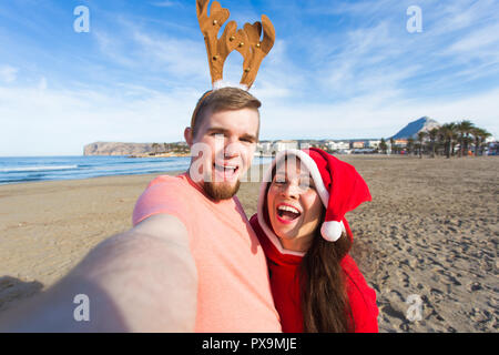 Spaß und Winterurlaub Konzept - glückliches Paar in Weihnachten Kostüme unter selfie über Sandstrand Hintergrund Stockfoto
