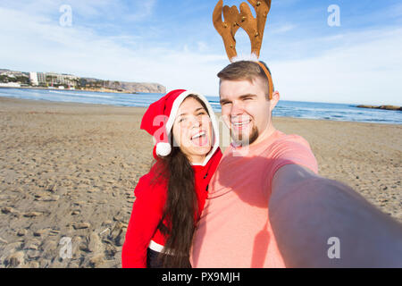 Spaß und Winterurlaub Konzept - glückliches Paar in Weihnachten Kostüme unter selfie über Sandstrand Hintergrund Stockfoto