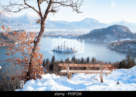 Wunderschöne Aussicht auf Holzbank mit Blick auf den berühmten Bleder See mit Insel und von Julischen Alpen im Hintergrund bei Sonnenaufgang im Winter, Slowenien Stockfoto