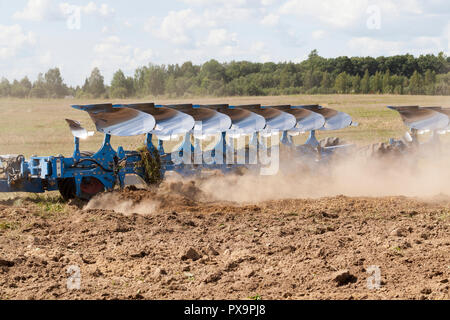 Die großen blauen Pflug pflügt den Boden auf dem Feld, eine Menge Staub aus dem trockenen Boden fliegt vom Pflug Stockfoto