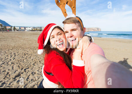 Spaß und Winterurlaub Konzept - glückliches Paar in Weihnachten Kostüme unter selfie über Sandstrand Hintergrund Stockfoto