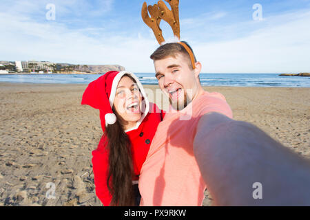 Spaß und Winterurlaub Konzept - glückliches Paar in Weihnachten Kostüme unter selfie über Sandstrand Hintergrund Stockfoto