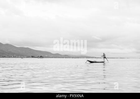 Reisen lokale junge burmesen männliche Fischer tragen geprüft, t-shirt, mit Stick und net zu fischen, Balancieren auf einem Fuß auf dem Boot, Inle Lake Myanmar, Birma Stockfoto