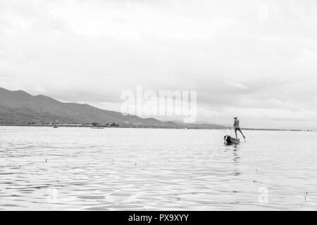 Reisen lokale junge burmesen männliche Fischer tragen geprüft, t-shirt, mit Stick und net zu fischen, Balancieren auf einem Fuß auf dem Boot, Inle Lake Myanmar, Birma Stockfoto