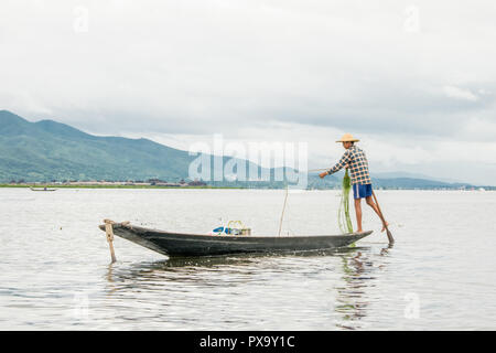 Reisen lokale junge burmesen männliche Fischer tragen geprüft, t-shirt, mit Stick und net zu fischen, Balancieren auf einem Fuß auf dem Boot, Inle Lake Myanmar, Birma Stockfoto