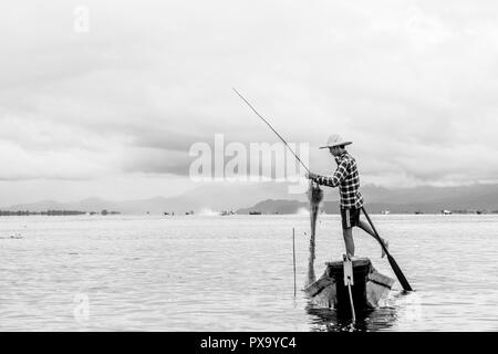 Reisen lokale junge burmesen männliche Fischer tragen geprüft, t-shirt, mit Stick und net zu fischen, Balancieren auf einem Fuß auf dem Boot, Inle Lake Myanmar, Birma Stockfoto