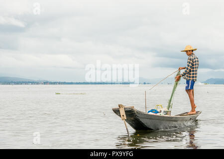 Reisen lokale junge burmesen männliche Fischer tragen geprüft, t-shirt, mit Stick und net zu fischen, Balancieren auf einem Fuß auf dem Boot, Inle Lake Myanmar, Birma Stockfoto