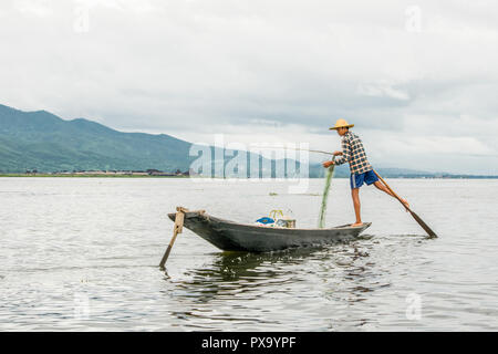 Reisen lokale junge burmesen männliche Fischer tragen geprüft, t-shirt, mit Stick und net zu fischen, Balancieren auf einem Fuß auf dem Boot, Inle Lake Myanmar, Birma Stockfoto