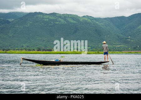 Lokale junge BURMESISCHE Fischer trägt ein kariertes Hemd Rückkehr nach Angeln, stehen am Rand eines dünnen tall Boot, rudern zurück, Inle See Stockfoto