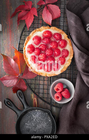 Rote Himbeere Butterkekse Tarte mit Vanille Pudding und verglaste frische Himbeeren auf Kühlung Rack dunkelbraunen Holzmöbeln rustikal Hintergrund. Ansicht von oben Stockfoto