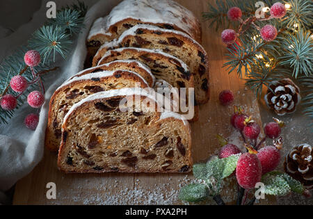 Christstollen auf darkfestive Hintergrund mit Tannen Zweigen, Lichter und und Beeren. Close-up auf dieser traditionellen deutschen Nachtisch für Weihnachten celebrat Stockfoto