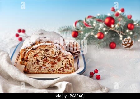 Christstollen auf Weiß-Blau festliche Hintergrund mit Tannen Zweigen und Nippes. Traditionelle deutsche Dessert für Weihnachten feiern. Stockfoto