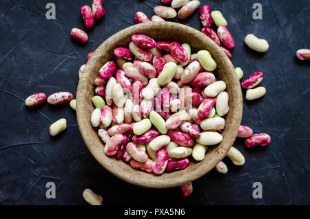 Frische organische lila Körner - Beens in Houten auf schwarzem Hintergrund. Weisse Bohnen vegan Protein Quelle. Ausgewogene Ernährung, Kochen, vegetarische und sauber Stockfoto