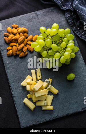 Käse Stück saftige Trauben und Walnüssen auf Schiefer. Stockfoto