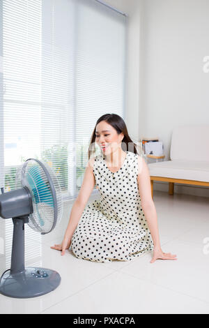 Schöne aisan Frau sitzt auf der Wohnzimmer Stock genießen Sie einen elektrischen Ventilator kühlen Wind. Stockfoto