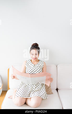 Jungen attraktiven asiatischen Frau liest Zeitung, beim Sitzen auf der Couch zu Hause Stockfoto