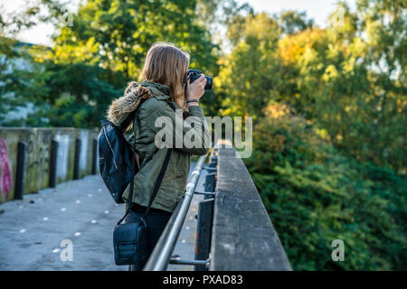 Eine junge Frau mit einer Kamera steht auf einer Brücke und nimmt ein Bild Stockfoto