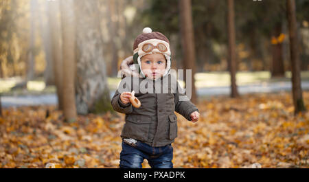 Little Boy in der pilot Cap spielen mit Spielzeug Flugzeug in den Park. Herbst. Stockfoto