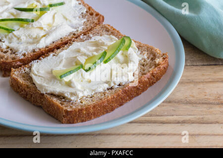 Hüttenkäse Brot - Scheiben Vollkornbrot mit Rahmspinat Hüttenkäse und Gurkenscheiben auf hölzernen Tisch Stockfoto