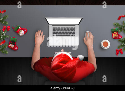 Mann hart Arbeiten am Laptop während der Weihnachtsfeiertage. Ansicht von oben Szene mit Weihnachtsbaum und Dekorationen. Kerl mit Santa Claus hat. Stockfoto