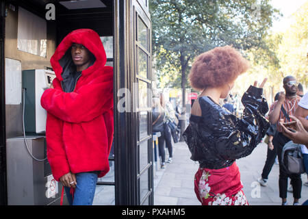 LONDON, Großbritannien - 14 September 2018: Leute auf der Straße, während der London Fashion Week. Ein Junge in einem rot Fellimitat Mantel in einer schwarzen Telefon starten Stockfoto