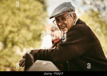 Portrait von Happy älterer Mann mit Brille und Deckel von einem holzgeländer mit einer Frau an der zurück in die PARK-Stellung. Lächelnd alter Mann im Park auf einem Winte Stockfoto