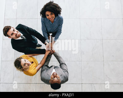 Corporate Business Professionals die Hände zusammen und sah in die Kamera lächelt. Multi-ethnischen Business Team mit Händen zusammen gestapelt Stockfoto