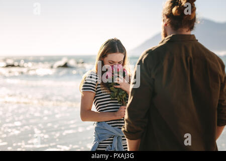 Schöne Frau duftende Blumen am Strand mit Freund. Frau lieben die überraschung von ihrem Freund gegeben. Liebespaar am Strand. Stockfoto