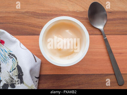 Joghurt in Schale aus Kunststoff schließen oben mit kleinen silbernen Löffel, Ansicht von oben Foto von Pfirsich Joghurt auf hölzernen Tisch Hintergrund Stockfoto