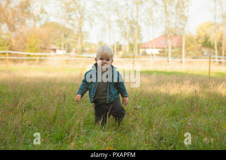 Weiß blond 1 Jahre alten Jungen posiert und auf eine Kamera auf weiten Feldern mit bunten Gras im Herbst Wetter. Wetter: sonnig und trocken. Stockfoto