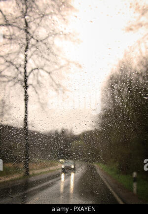 Ein Auto mit Scheinwerfern gesehen durch ein Regentropfen - überdachte Windschutzscheibe. Stockfoto