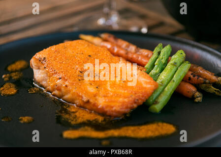 Lachs auf einer Platte mit Karotten und Spargel auf einer schwarzen Platte gewartet. Stockfoto