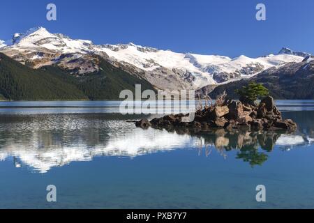 Isolierte Kiefer auf Rock Island. Schneebedeckte Berggipfel Garibaldi Lake Calm Water Reflections. Malerische Landschaft Coast Mountains BC Kanada Stockfoto