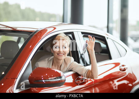 Überglücklich Treiber Frau lächelnd und zeigt neue, während Sie sich im Autohaus sitzen Stockfoto