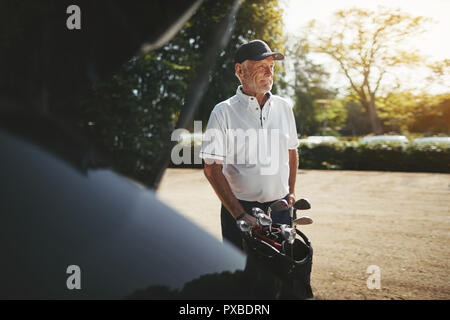 Lächelnd älterer Mann Verpackung seine Vereine in den Kofferraum seines Autos nach dem Spielen Sie eine Runde Golf auf einem sonnigen Nachmittag Stockfoto