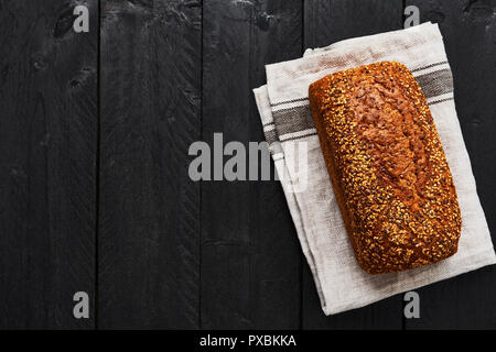 Laib Vollkornbrot auf grau Geschirrhandtuch über schwarzen Holztisch. Ansicht von oben mit der Kopie. Stockfoto