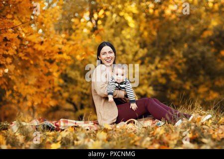 Fröhliche Mutter mit Baby Junge spielt im Herbst Park. Schöne Frau ihren kleinen Sohn im Freien Holding Stockfoto