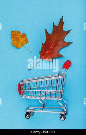 Trolley mit Blättern auf blauem Hintergrund. Konzept zum Thema herbst Rabatte, Ansicht von oben Stockfoto