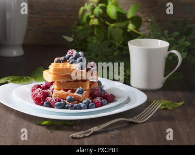 Leckere süße Waffeln mit Himbeeren und Blaubeeren auf einem alten Holztisch. Stockfoto