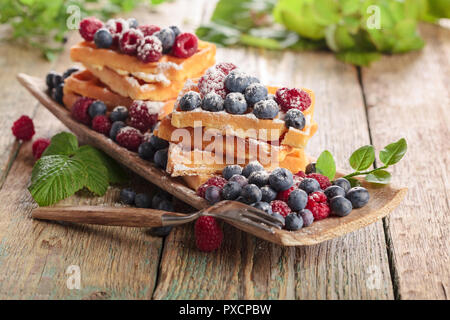Leckere süße Waffeln mit Himbeeren und Blaubeeren auf einem alten Holztisch. Stockfoto